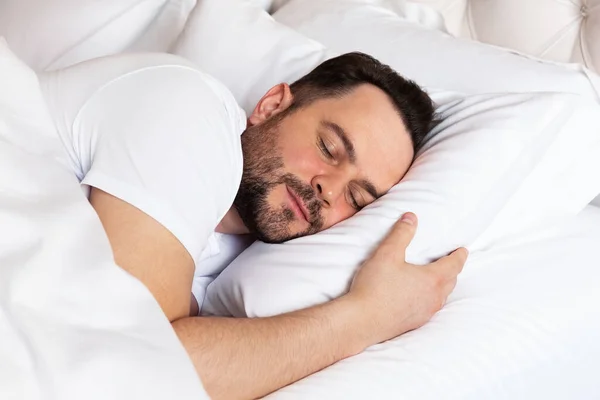 Handsome young man sleeping on white bed linen. View of handsome smiling man  sleeping in his bed at home.