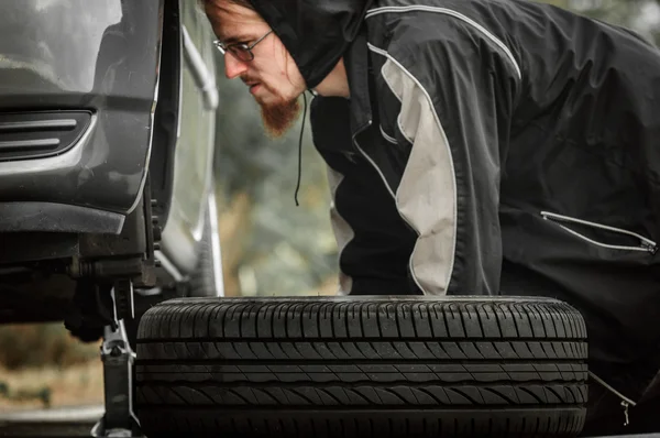 Adulto joven inspeccionando la rueda de un coche — Foto de Stock