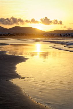 Famara Sahili 'nde günbatımı. Lanzarote Kanarya Adaları Caleta de Famara, Famara Sahili Rüzgar sörfü ve akşam güneşinde sörf plajı.
