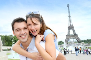 Man carrying girlfriend on his back in front of Eiffel tower