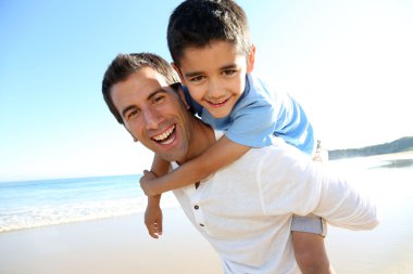 Father holding son on his shoulders at the beach clipart