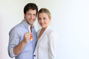 Yeni evlerinin anahtarlarını tutan gülümseyen genç çift.