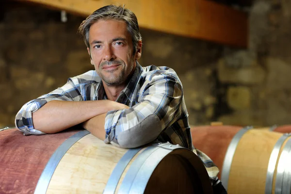 Smiling winemaker leaning on wine barrel in winery — Stock Photo, Image
