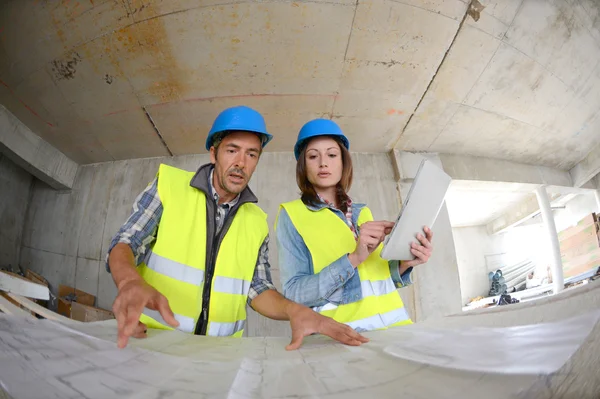 Workteam checking blueprint inside house under construction — Stock Photo, Image