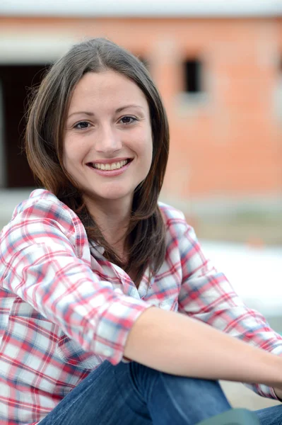 Vrolijke vrouw zitten voor huis in aanbouw — Stockfoto