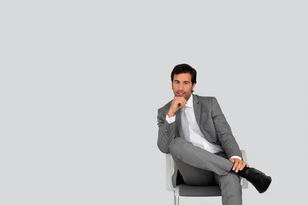 Geschäftsmann sitzt auf Stuhl vor grauem Hintergrund — Stockfoto
