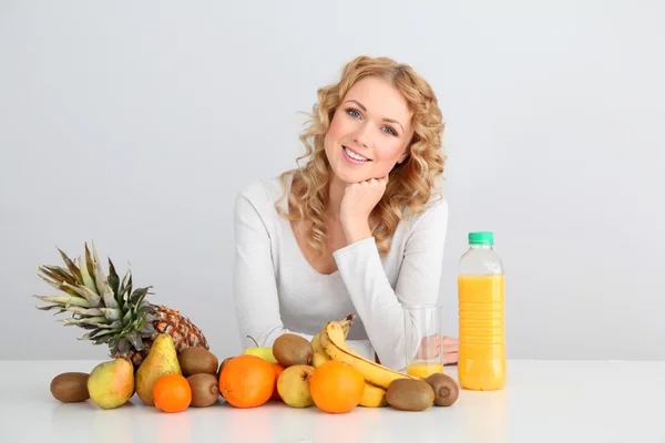 Femme blonde souriante assise avec des fruits sur la table — Photo