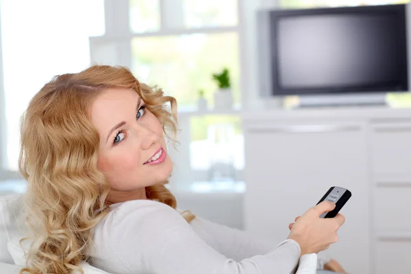 Piękne blond kobieta siedzi w kanapie oglądając tv — Zdjęcie stockowe