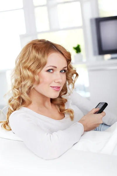 Beautiful blond woman sitting in sofa watching tv — Stock Photo, Image