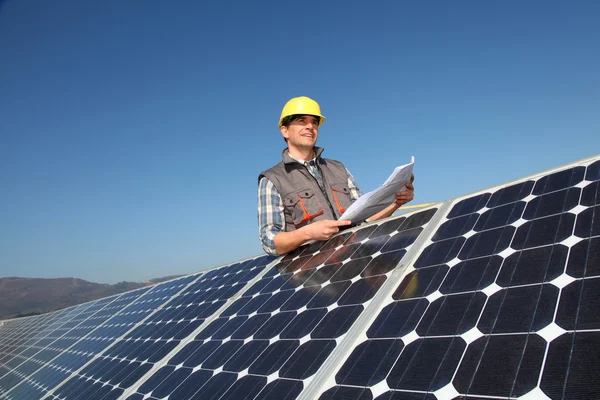 Hombre de pie junto a paneles solares con plan de construcción —  Fotos de Stock