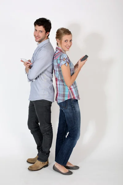 Ungt par standng rygg mot rygg med mobiltelefon — Stockfoto