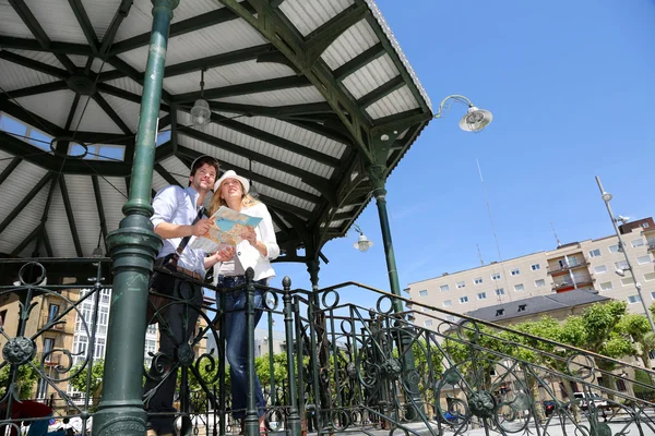 Young couple standing in gazebo reading touristic map — Stock Photo, Image