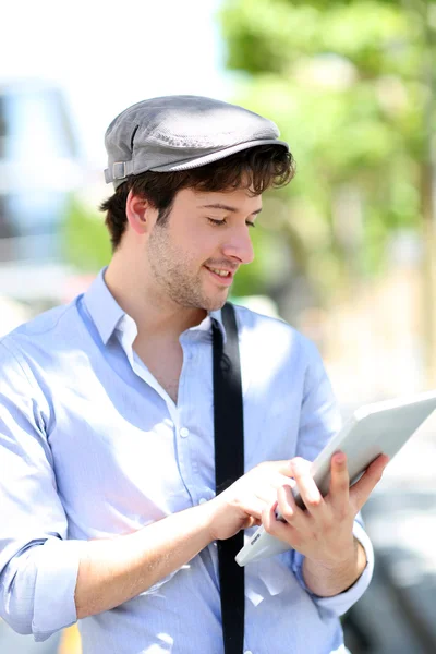 Junger Mann mit Hut mit digitalem Tablet in der Stadt — Stockfoto