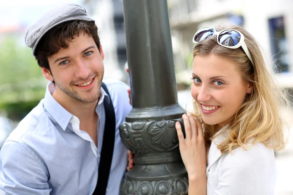 Retrato de casal alegre em pé junto ao poste de iluminação na cidade — Fotografia de Stock