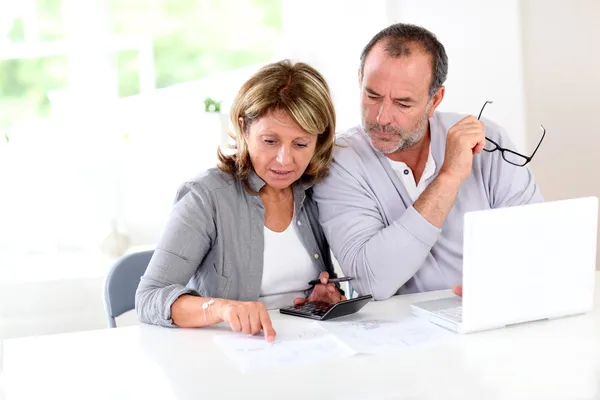 Couple reading construction plan at home with use of laptop — Stock Photo, Image