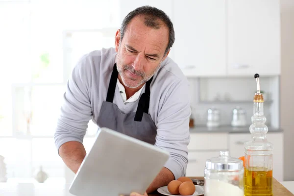 Homem sênior na cozinha usando tablet eletrônico — Fotografia de Stock