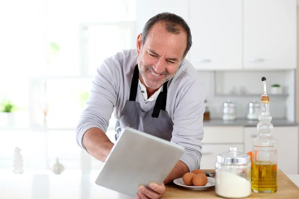 Hombre mayor en la cocina usando tableta electrónica — Foto de Stock