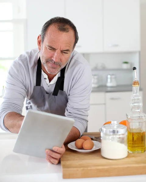 Äldre man i köket med hjälp av elektroniska tablett — Stockfoto