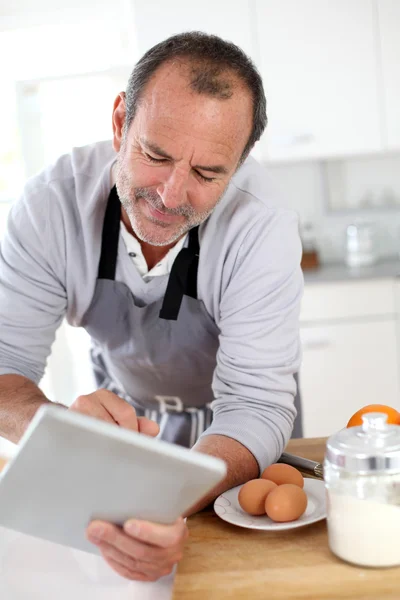 Homem sênior na cozinha usando tablet eletrônico — Fotografia de Stock