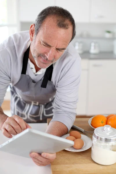 Hombre mayor en la cocina usando tableta electrónica — Foto de Stock