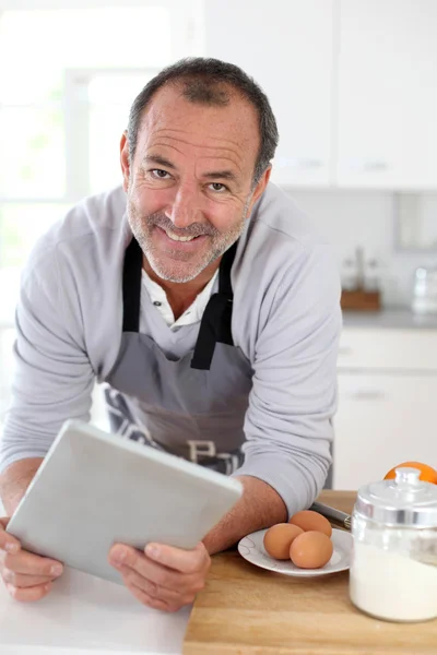 Hombre mayor en la cocina usando tableta electrónica — Foto de Stock