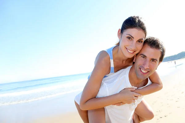 Man carrying girlfriend on his back at the beach — Stock Photo, Image