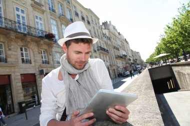 Young man with hat in town using electronic tablet