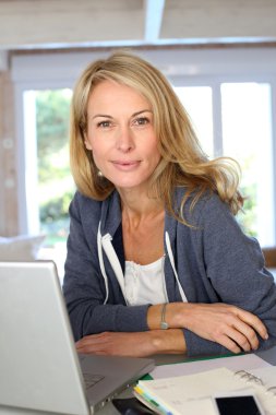 Orta yaşlı sarışın bir kadın evde laptop ile çalışma