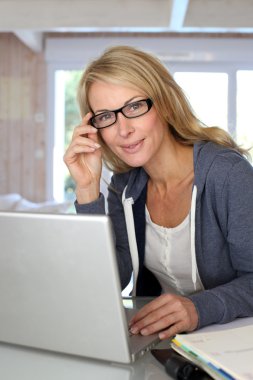 Orta yaşlı sarışın bir kadın evde laptop ile çalışma