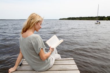 kadın göl tahta üzerinde oturup kitap okuma