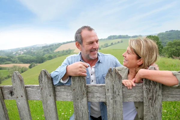 Senior couple leaning on fence in countryside — Stock Photo, Image