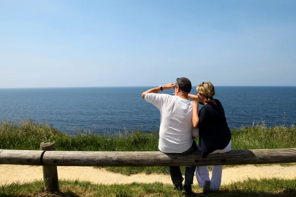 Couple sitting on fence enjoying panoramic sea view — Stock Photo, Image