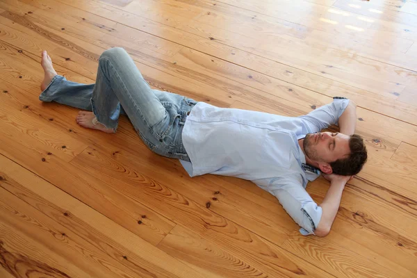 Hombre joven relajándose en el piso de madera en el apartamento —  Fotos de Stock