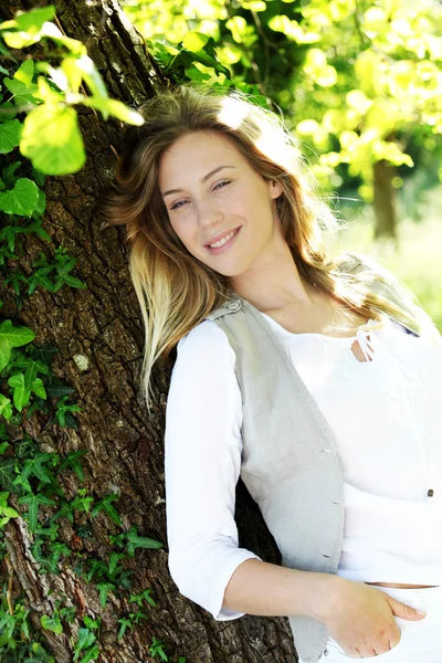 Mujer rubia sonriente apoyada en el árbol —  Fotos de Stock