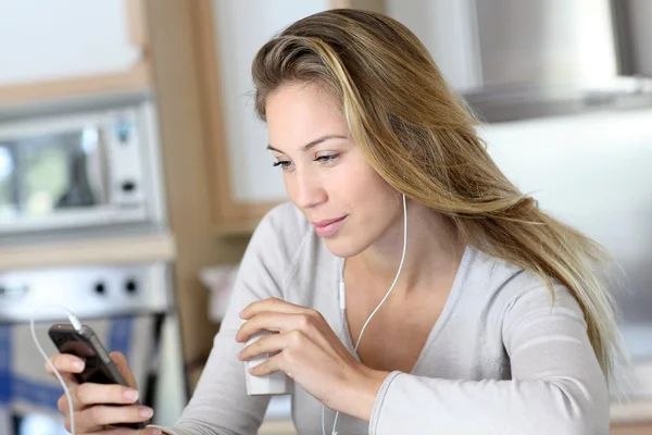 Jovem mulher usando smartphone em casa com fones de ouvido — Fotografia de Stock