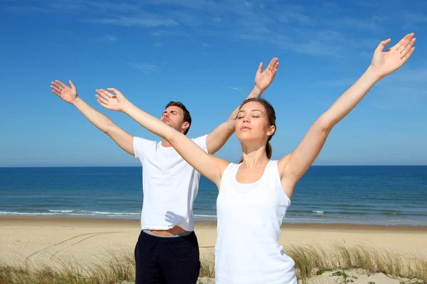 Paar mediteren op het strand met armen omhoog — Stockfoto