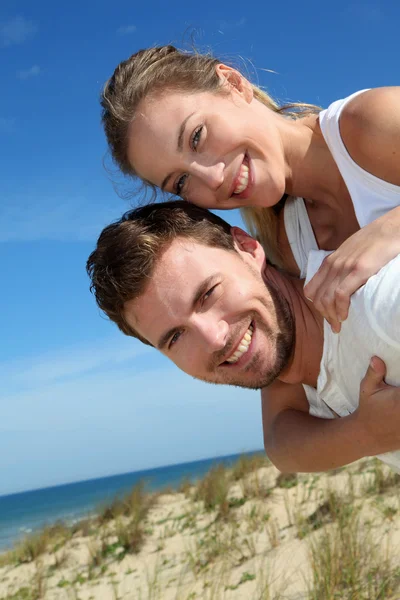 Man giving piggyback ride to girlfriend on a sand dune — Stock Photo, Image