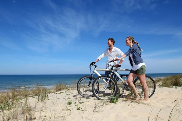 Casal de pé em uma duna de areia com bicicletas — Fotografia de Stock