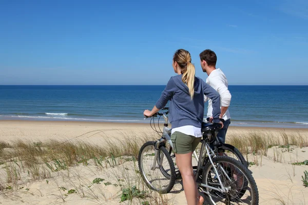 Casal de pé em uma duna de areia com bicicletas — Fotografia de Stock