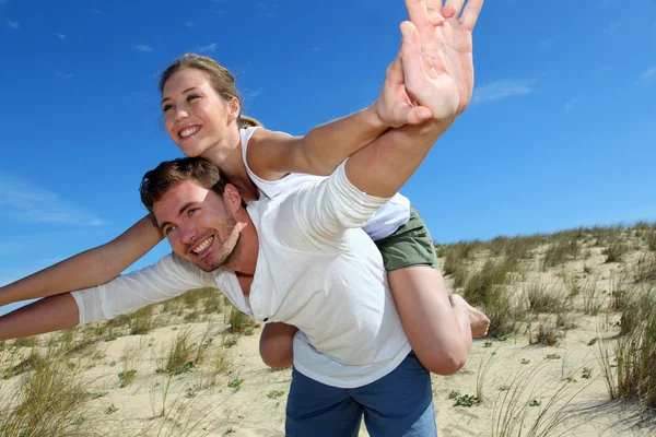 Homme donnant tour de dos de porc à petite amie sur une dune de sable — Photo