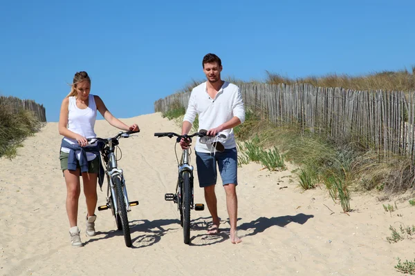 Couple walking on a sandy path with bicycles — Stock Photo, Image