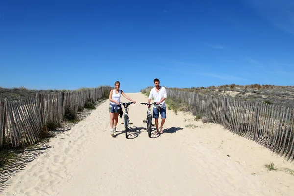 Couple walking on a sandy path with bicycles — Stock Photo, Image