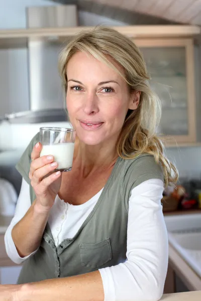 Porträt einer blonden Frau, die in der heimischen Küche Milch trinkt — Stockfoto