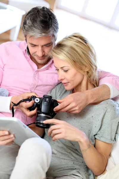 Casal em casa olhando para fotos em tablet eletrônico — Fotografia de Stock