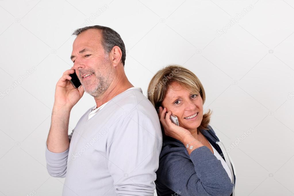 Senior couple standing back to back and using mobile phone