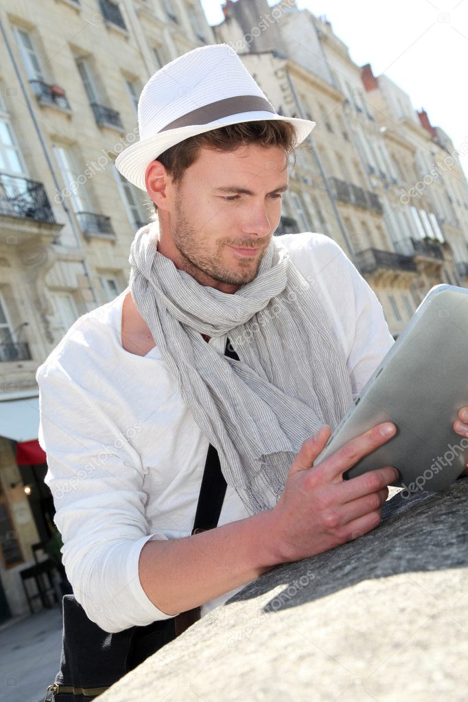 Young man with hat in town using electronic tablet