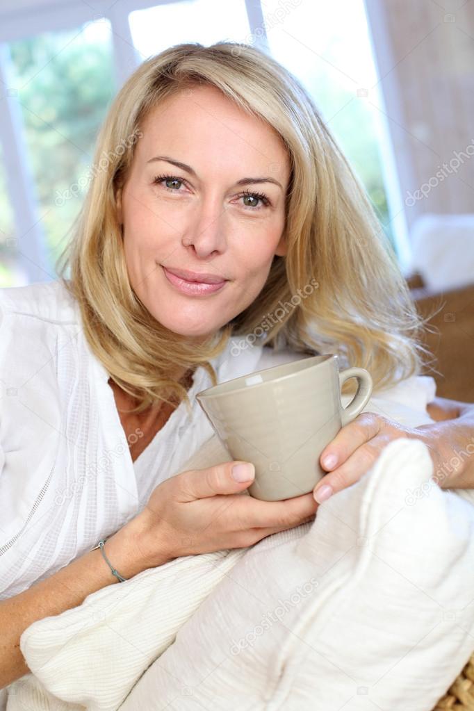 Mature blond woman in couch having a tea