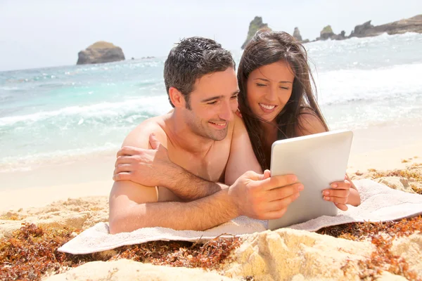 Ζευγάρι στην παραλία χρησιμοποιώντας ηλεκτρονικό, ταμπλετών — Φωτογραφία Αρχείου