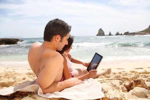 Pareja en la playa usando tableta electrónica — Foto de Stock