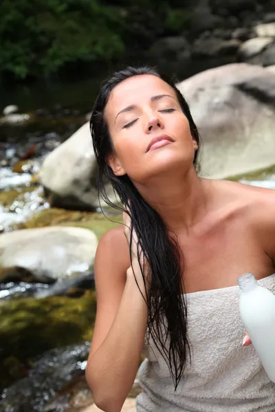 Beautiful young woman applying hair conditioner sitting by river — Stock Photo, Image